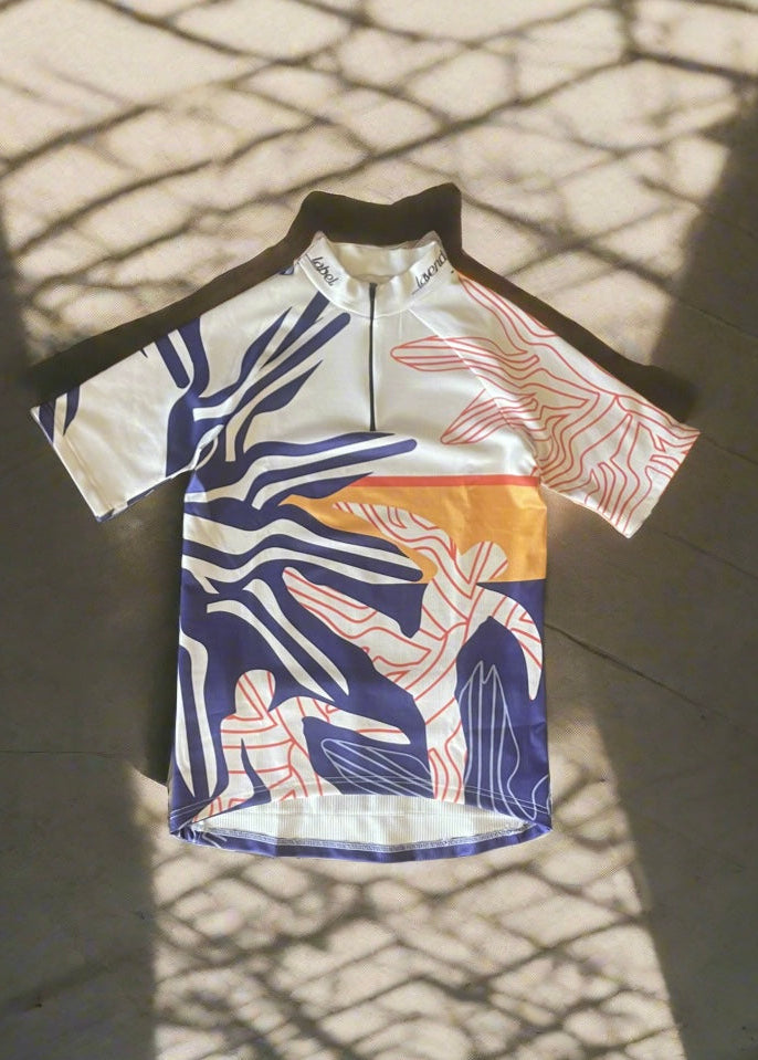 A short-sleeved cycling jersey with a geometric pattern, predominantly in blue and white colors, displayed on a flat surface.