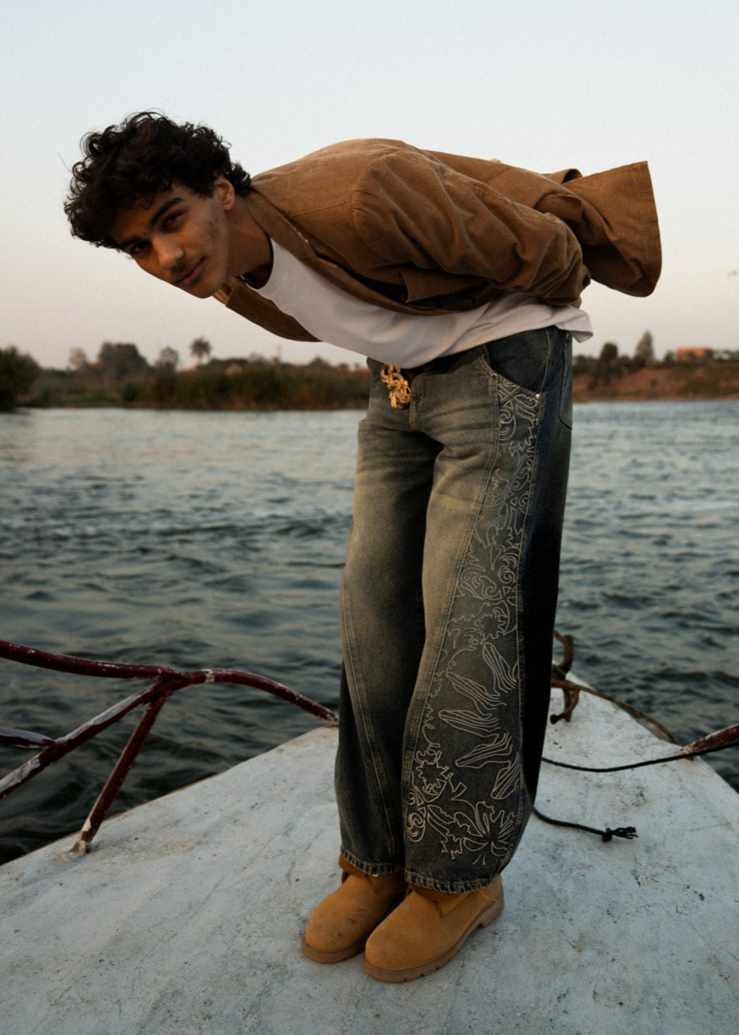 Person standing on a dock by a body of water with a jacket over their shoulder.
