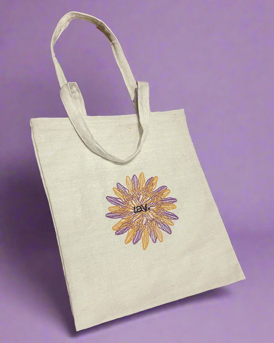 A beige tote bag with embroidered floral and geometric patterns in the center, displayed against a purple background.