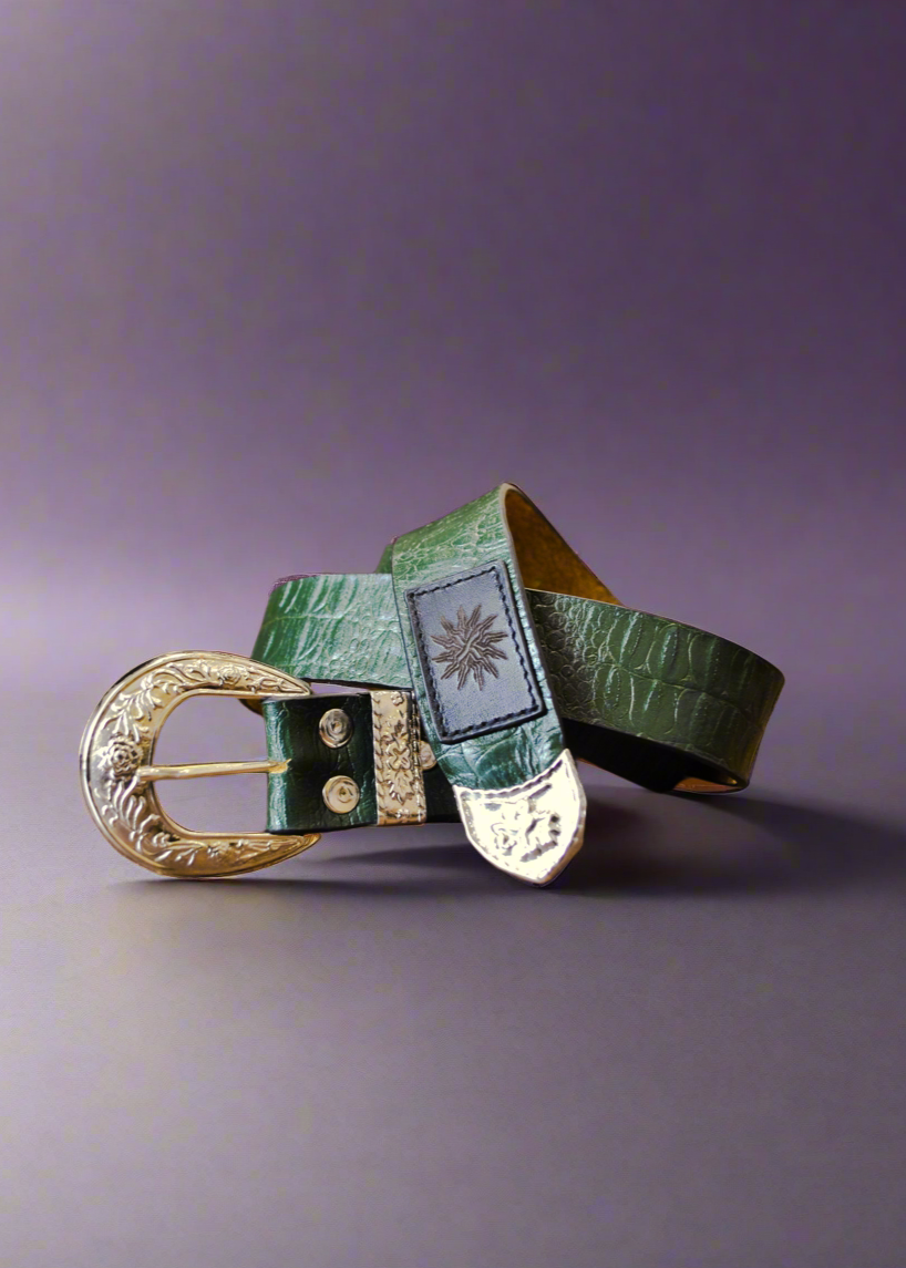 A green cowhide leather belt with detailed silver hardware, including a buckle and embossed branding, displayed against a purple background.