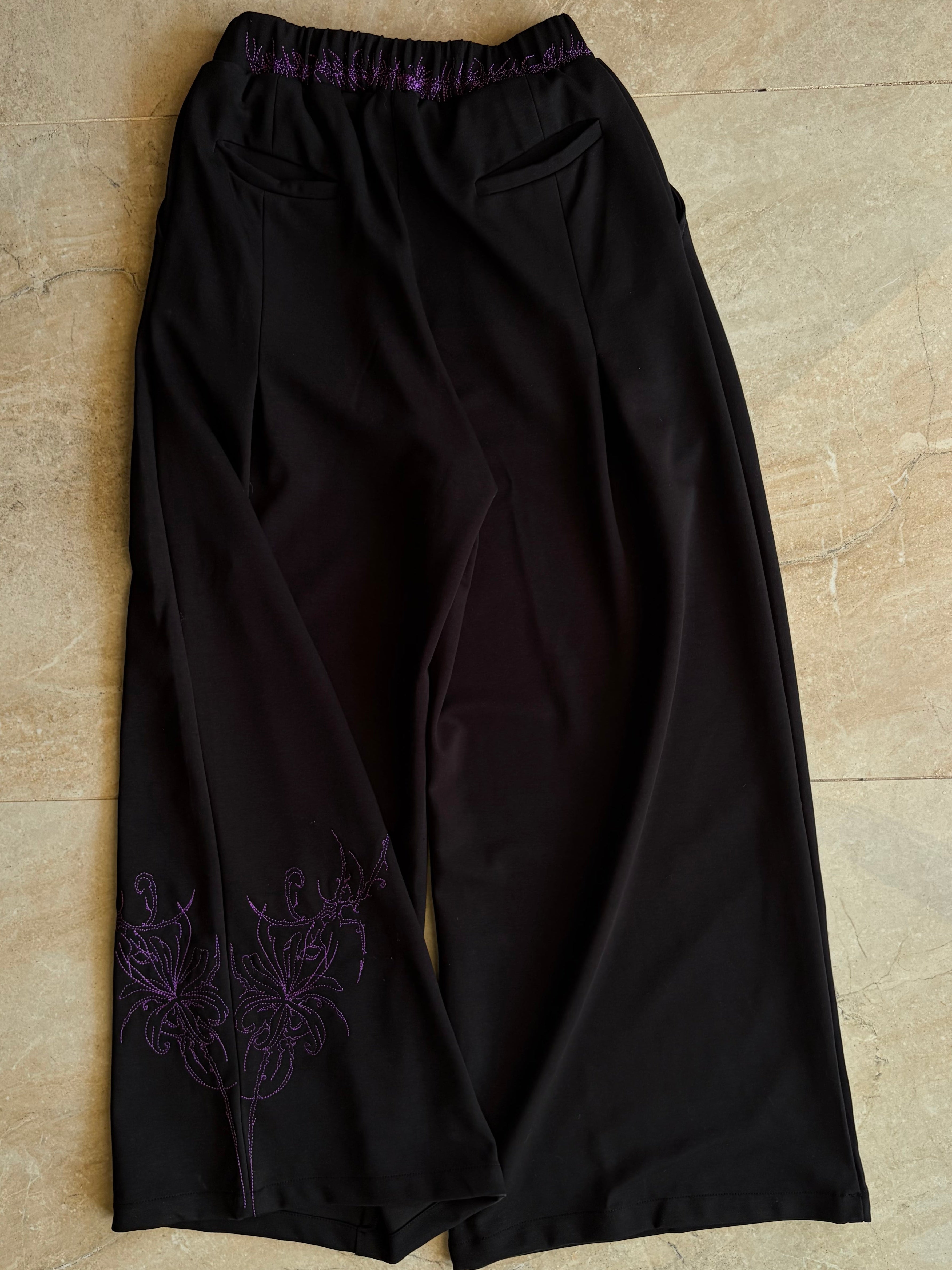 Black pants with purple embroidery on a beige tiled floor