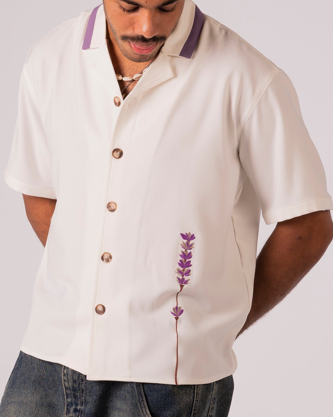 Man wearing a beige short-sleeve shirt with a floral design on a plain background