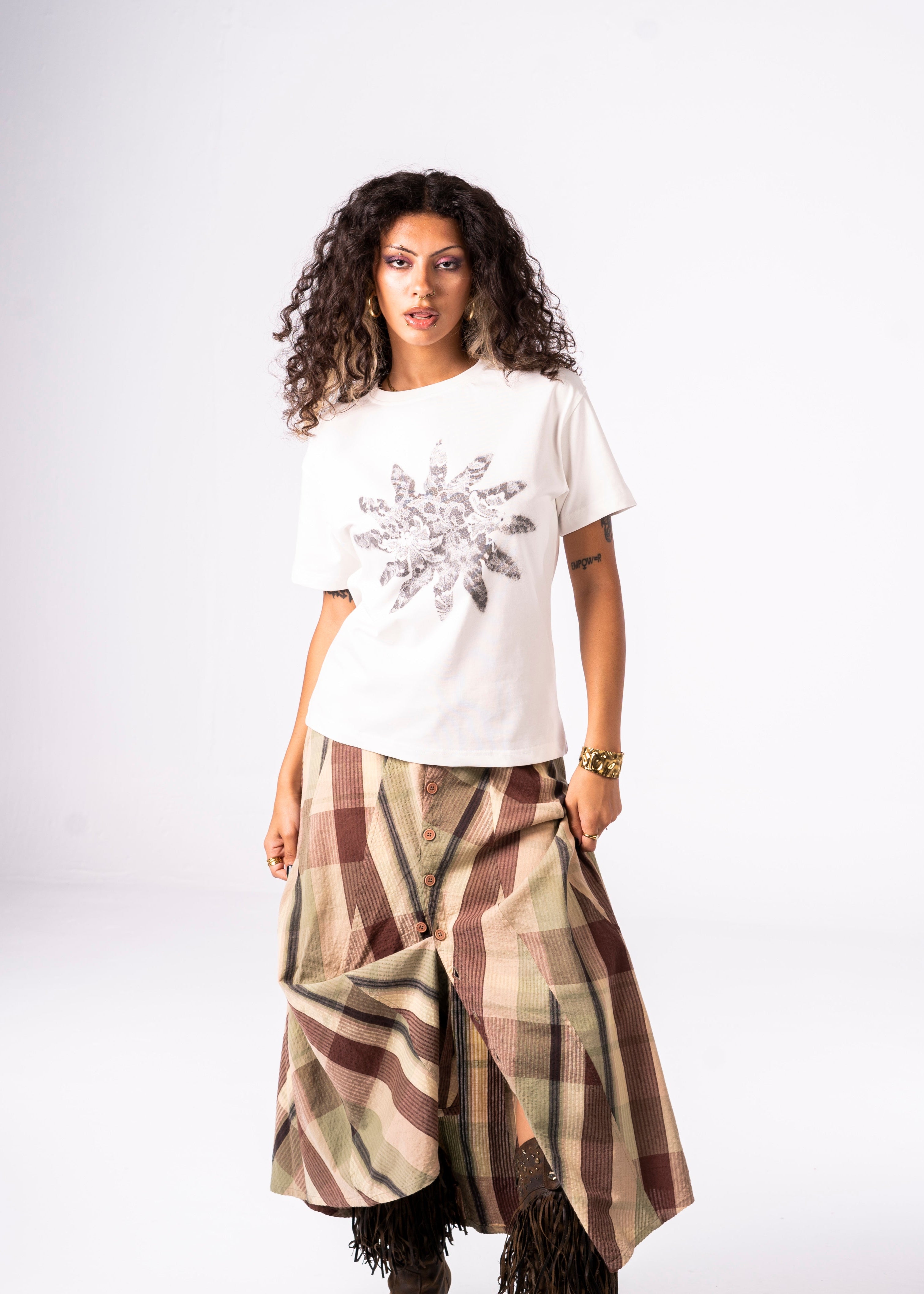 Woman wearing a white t-shirt with a floral design and a plaid skirt on a white background