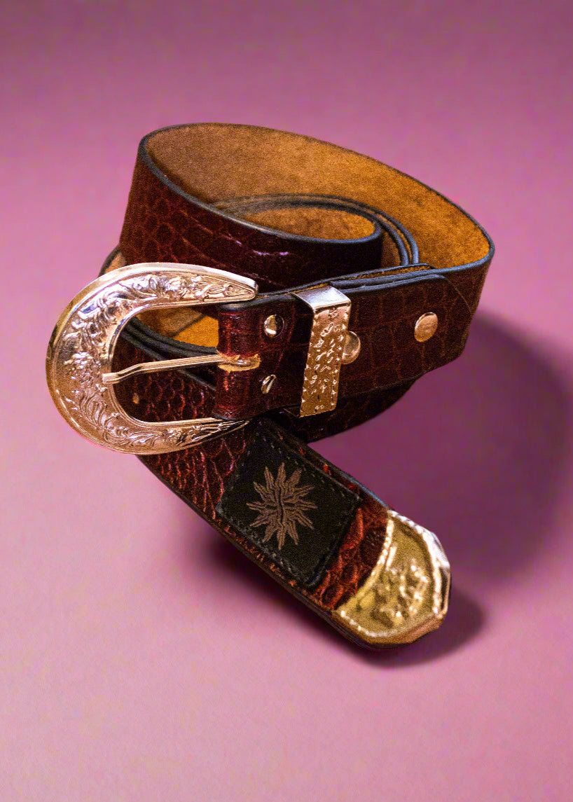 A brown leather belt with detailed silver hardware, including a buckle and a tassel, displayed against a pink background.